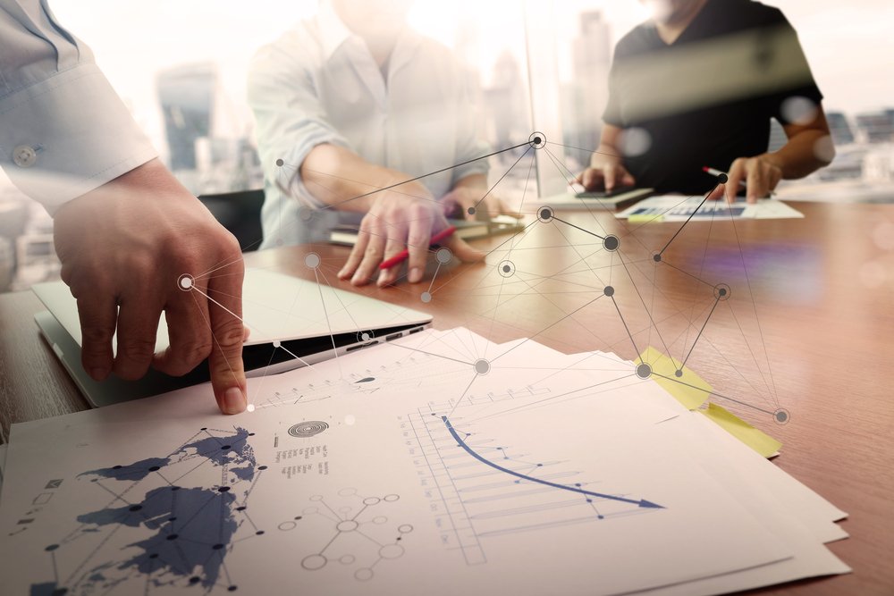 business documents on office table with smart phone and laptop computer and graph financial with social network diagram and two colleagues discussing data in the